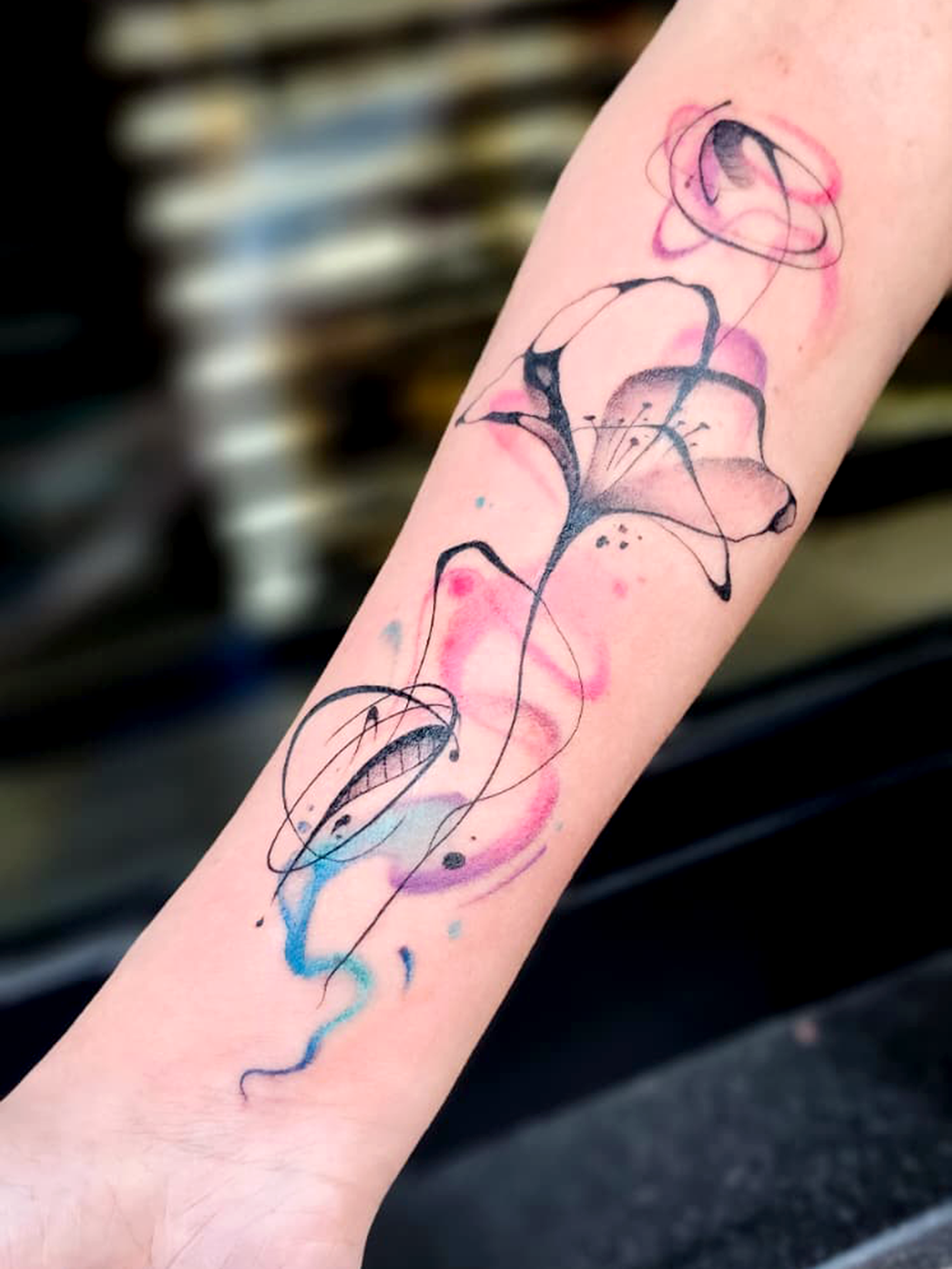 Tatuaggio floreale con linee nere e pennellate rosa e azzurre.