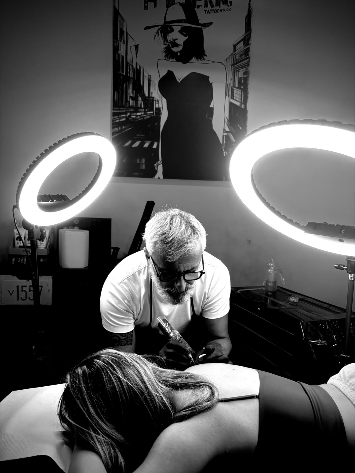 Marcello Scavo tatua in studio, illuminato da due lampade ad anello.
