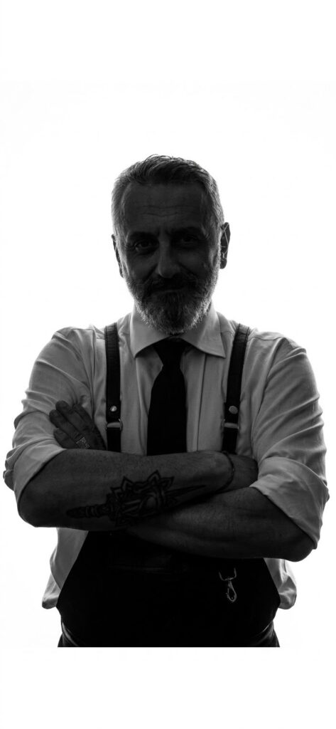 Marcello Scavo, a braccia conserte, in camicia e bretelle su sfondo bianco.